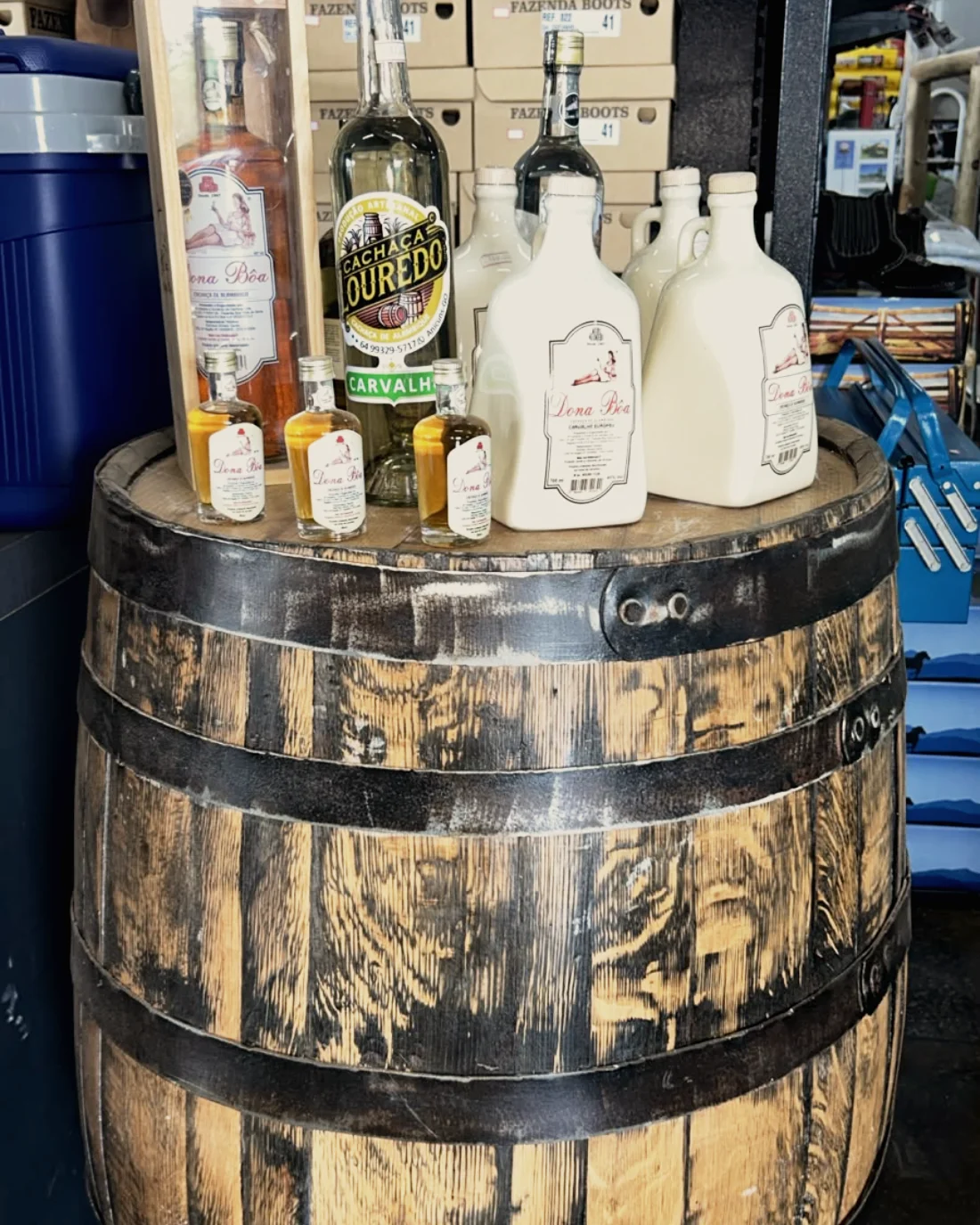 Cachaça artesanal em cima de um barril de carvalho, com caixas de botina ao fundo